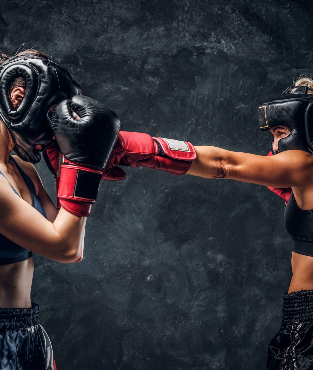 Process of fight between two female boxers in gloves and helmets over dark background.